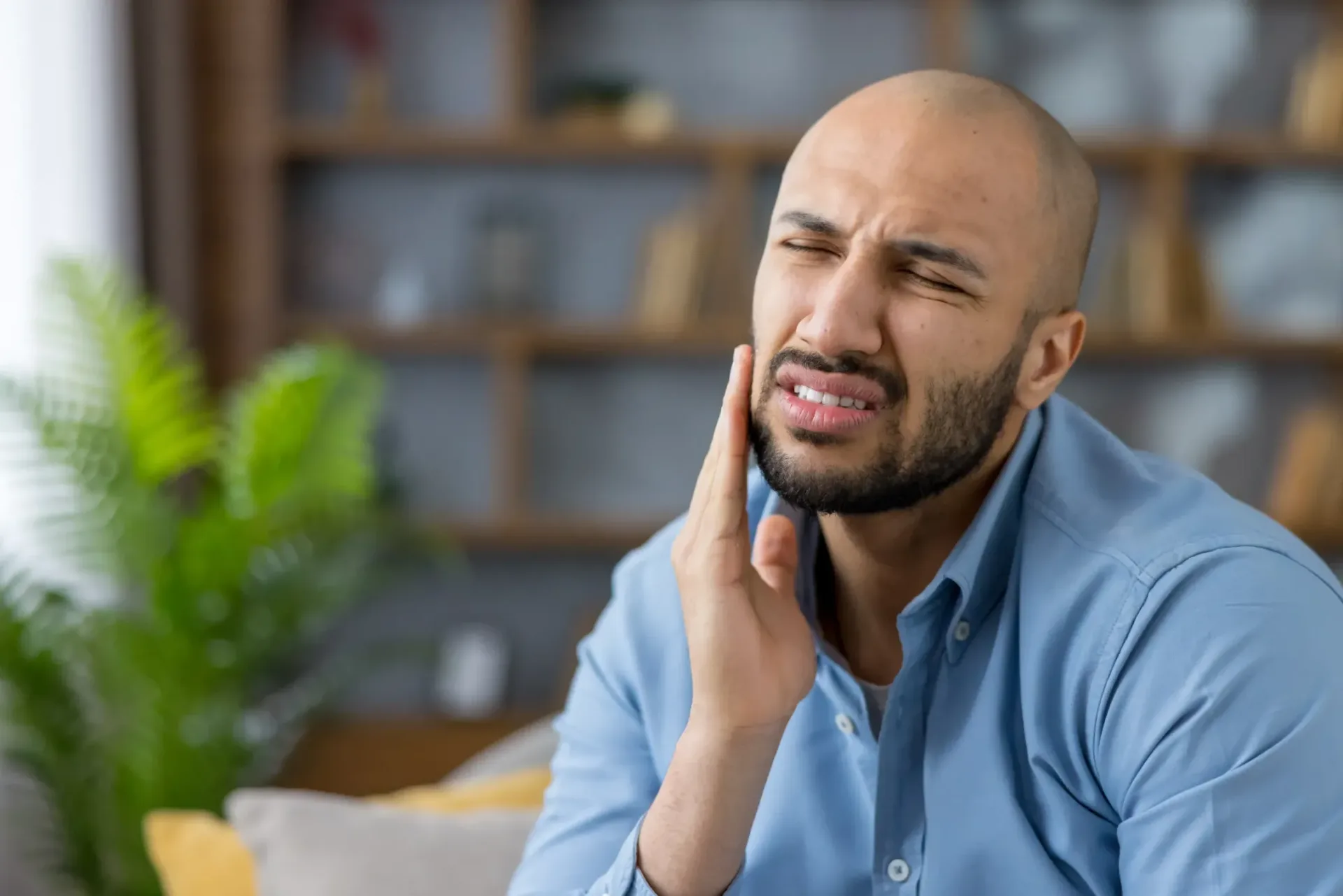 Man wincing and holding his jaw from sudden tooth pain